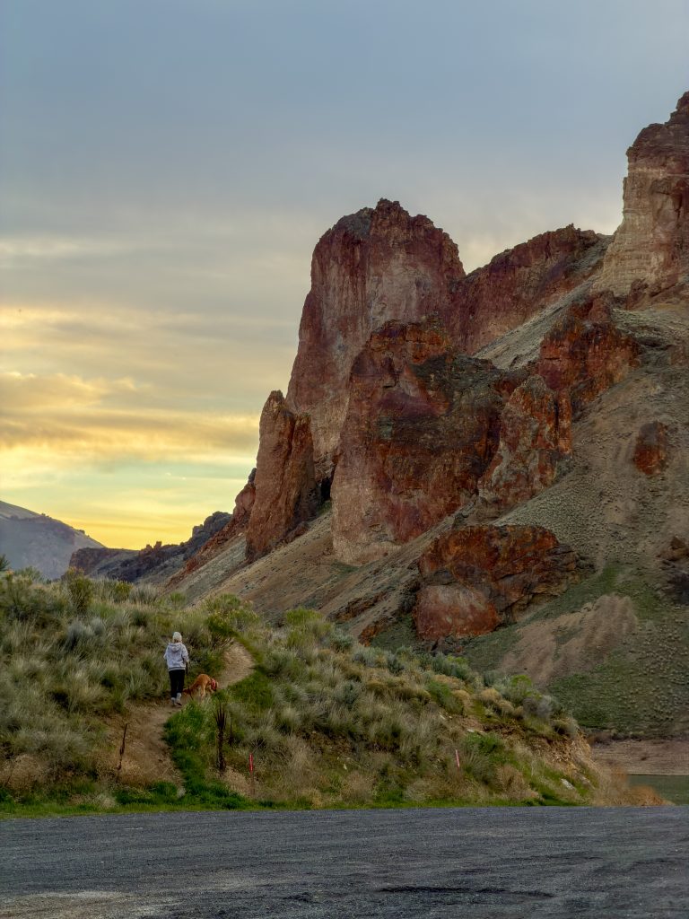 Woman walking with a golden retriever beneath the rock formations at Leslie Gulch, Oregon